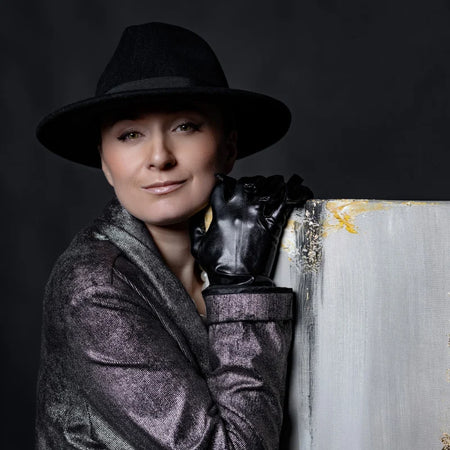 Person wearing a black hat and coat, holding a paintbrush against a dark background