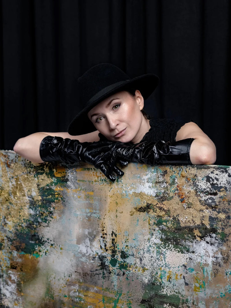 Woman wearing a black hat and gloves leaning on a textured surface with a dark background