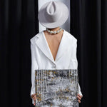 Person wearing a white outfit and hat holding a textured painting against a black background